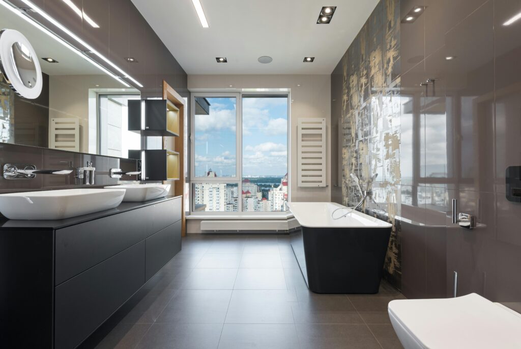 Wooden furniture with bathtub and ceramic sinks and toilet bowl in contemporary master bathroom with big windows in daylight